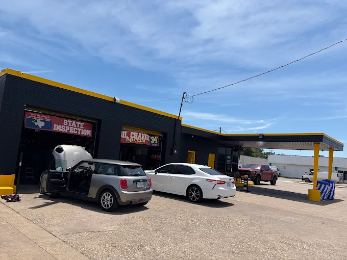 Exterior of Tune Ups R Us in Garland, Texas — yellow-trimmed black building with State Inspection and Oil Change Special banners