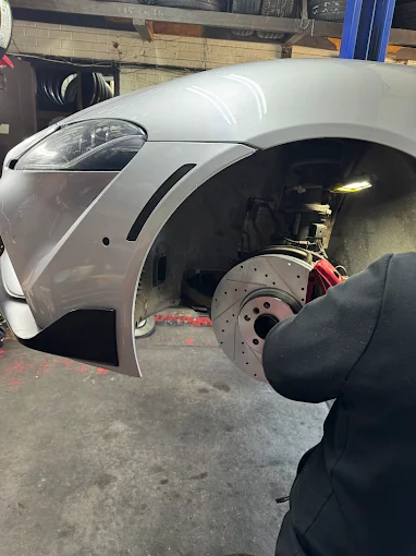 Drilled and slotted brake rotor with red caliper on a white Toyota Supra in the shop bay